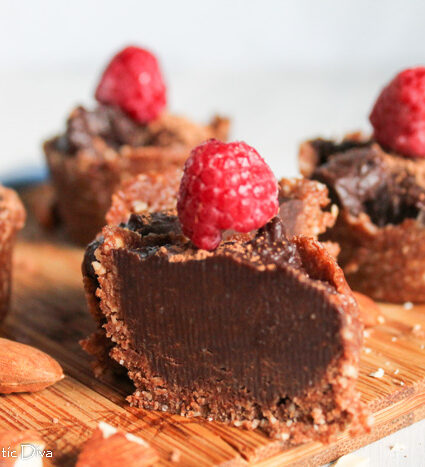 an arrangement of raw chocolate tarts topped with a raspberry atop a bamboo cutting board