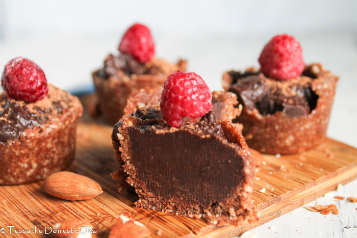 an arrangement of raw chocolate tarts topped with a raspberry atop a bamboo cutting board