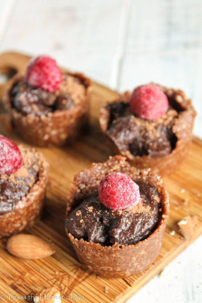 overhead view of several no bake chocolate tarts in a raw nut crust with raspberry on top