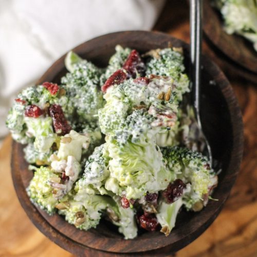 dark wooden bowls fillled with broccoli florets in a creamy sauce with chopped bacon, cranberries, and sunflower seeds