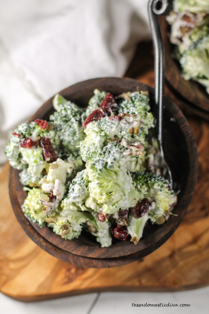 dark wooden bowls fillled with broccoli florets in a creamy sauce with chopped bacon, cranberries, and sunflower seeds