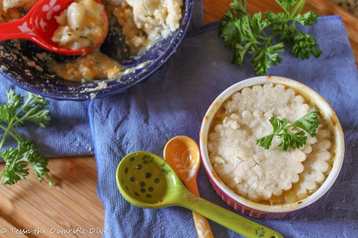 birds eye view of mini pastry topped chicken pot pies atop a bamboo cutting board with a periwinkle cloth and colorful ceramic spoons