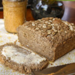 a sliced loaf of gluten free oatmeal bread on a pale yellow cloth with jam in background