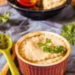 a grape colored ramekin filled with a mini chicken pot pie topped with parsley atop a periwinkle blue linen