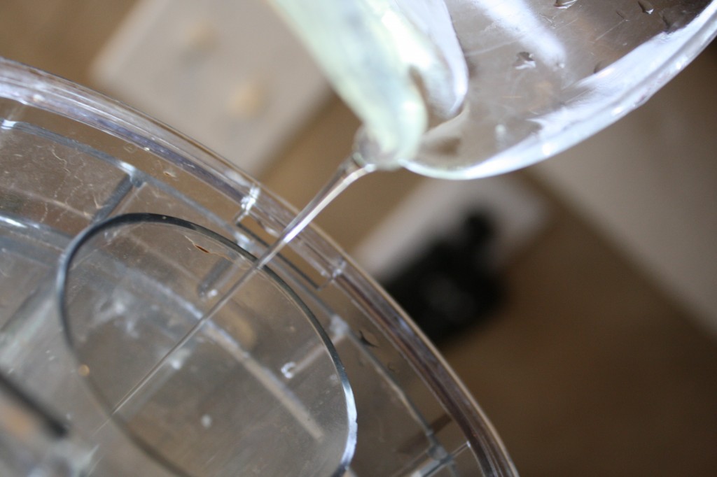 a thin stream of avocado oil pouring through a food processor spout for homemade mayonnaise