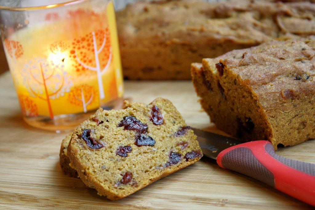 sliced mini loaves of pumpkin bread studded with dried cranberries on a bamboo cutting board and a glowing candle