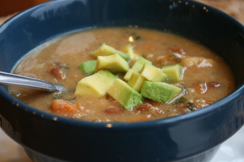 eye level view of a savory pinto bean and sweet potato chili with fresh chopped avocado in a blue bowl