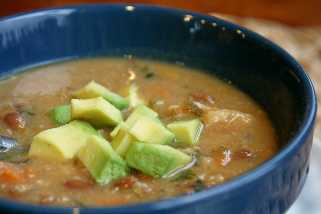 a blue bowl close up of pinto bean and vegetable chicken chili topped with chopped avocado