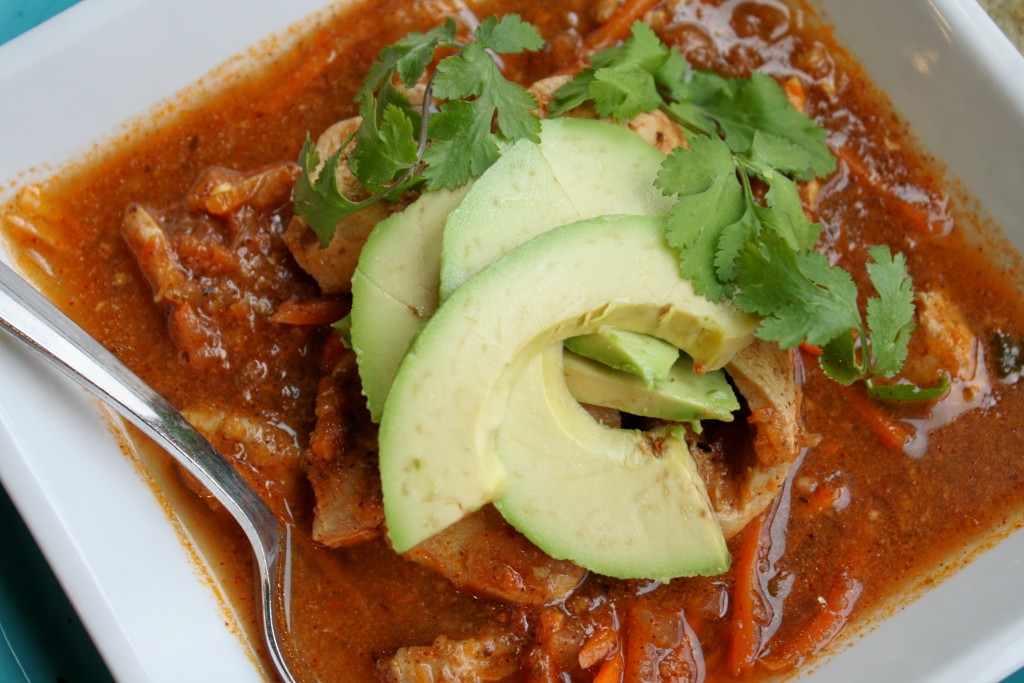 closeup overhead shot of a square white bowl filled with a mexican tomato broth soup garnished with fresh cilantro and avocado slices