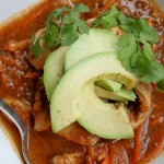 birdseye view of a white bowl filled with a savory mexican tomato broth topped with sliced avocado and cilantro