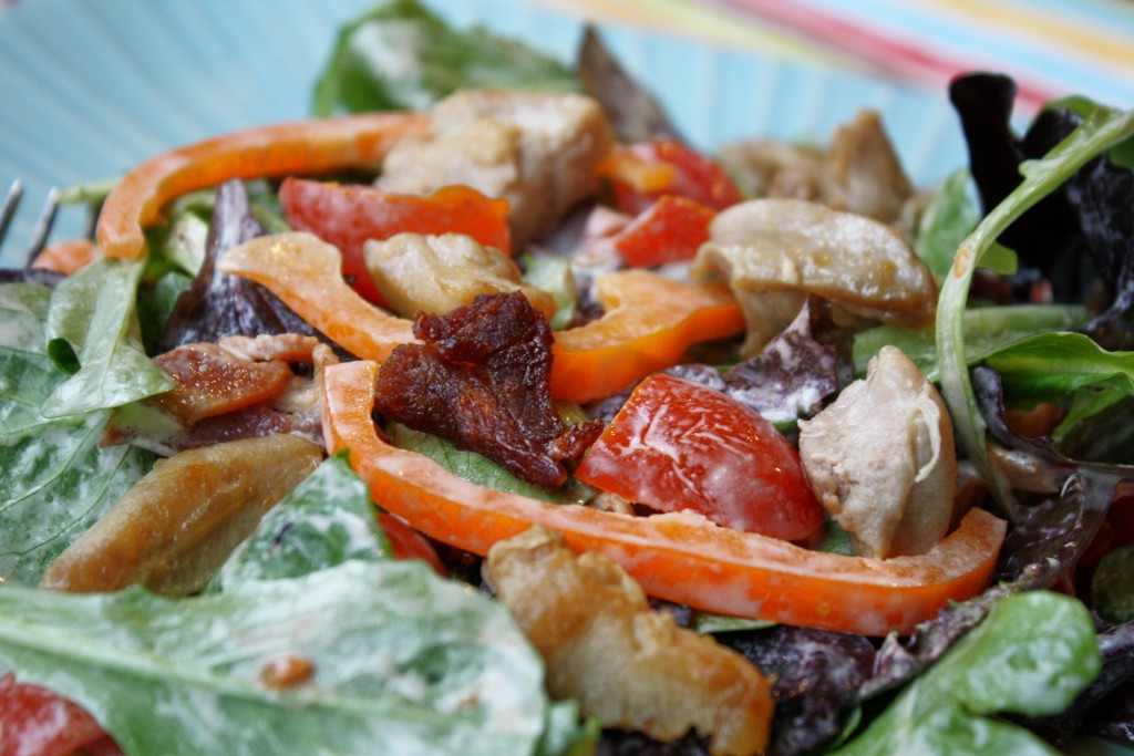 a up close view of a blt salad with a creamy mayo dressing, bacon, tomato, and crispy chicken thighs