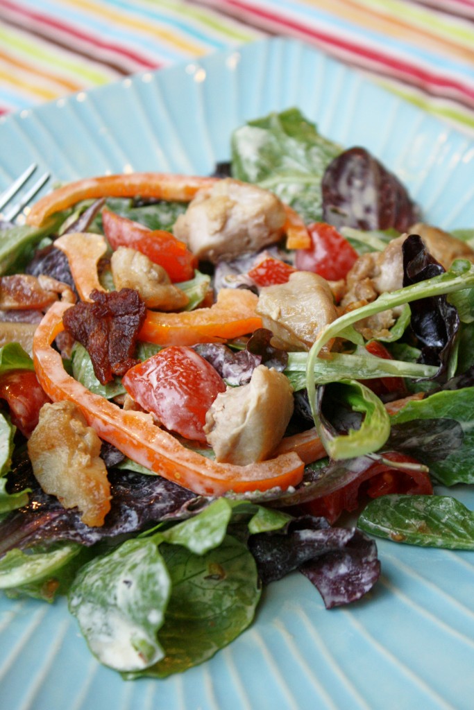 chicken blt salad topped with bell peppers and tomatoes on a light blue plate and a festive striped cloth