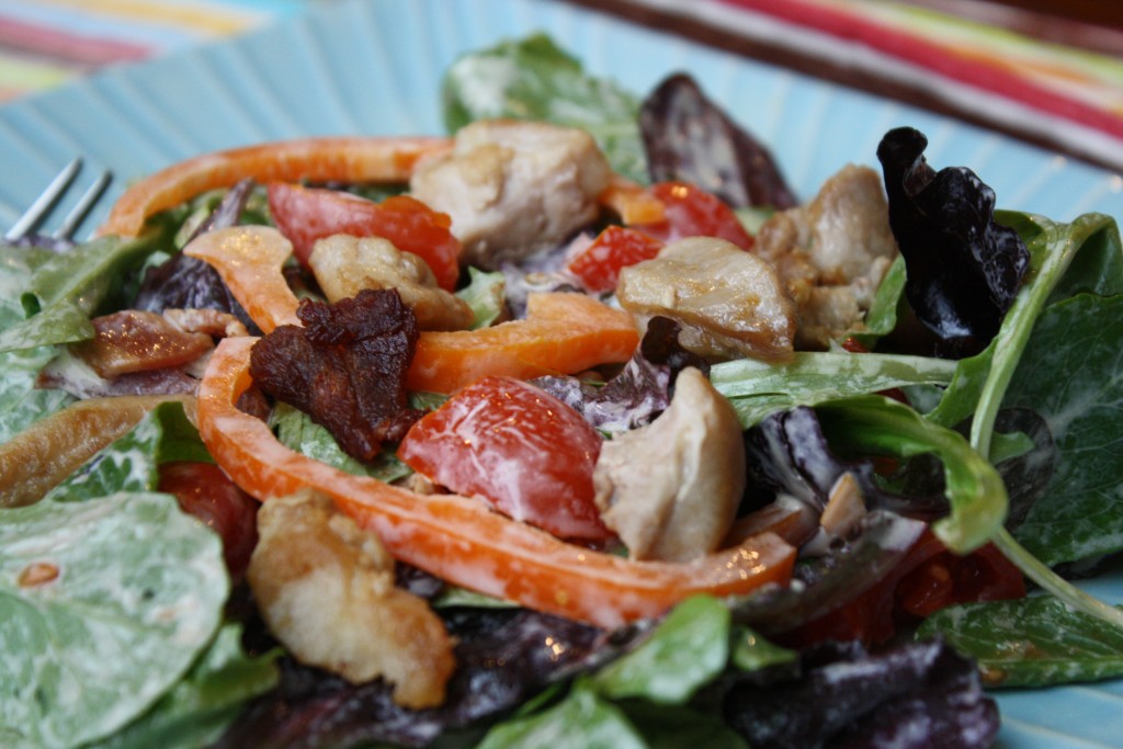 close up of a blue plate with creamy coated salad greens with peppers, chicken, bacon, and tomatoes