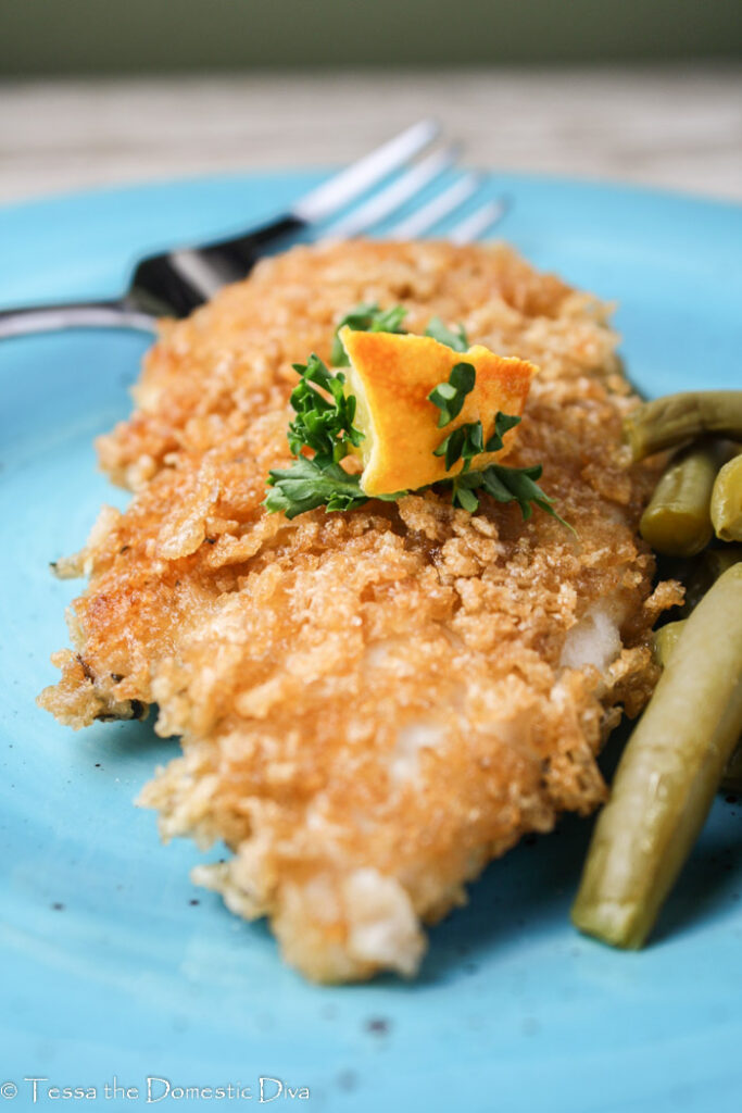 gluten free panko crusted chicken breast with a wedge of lemon and fresh parsley on a blue plate