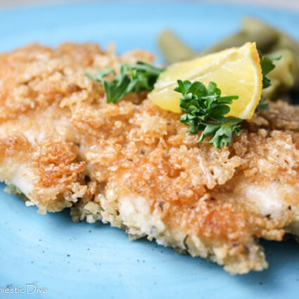 a gluten and egg free panko crusted chicken breast from eye level on a turquoise plate topped with a lemon wedge and chopped parsley