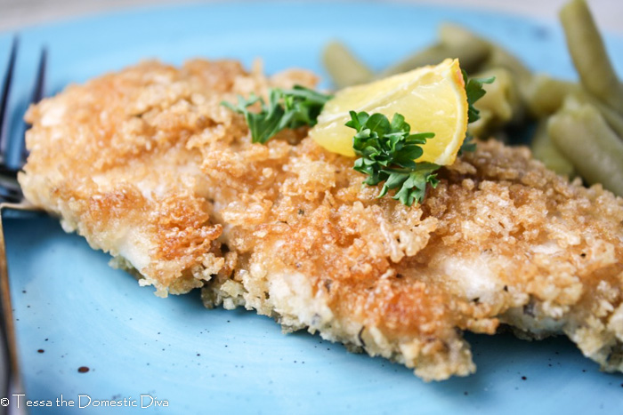 a gluten and egg free panko crusted chicken breast from eye level on a turquoise plate topped with a lemon wedge and chopped parsley