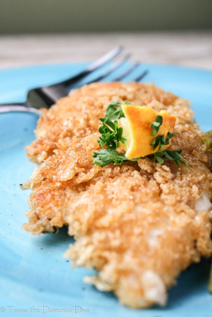 crispy coated chicken breast topped with lemon and parsley garnish