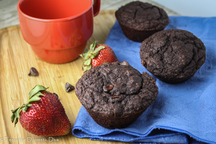 three chocolate muffins arranged on a periwinkle linen with fresh strawberry