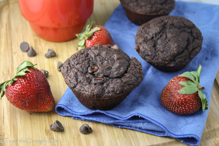two chocolate muffins arranged on a cutting board with fresh strawberries