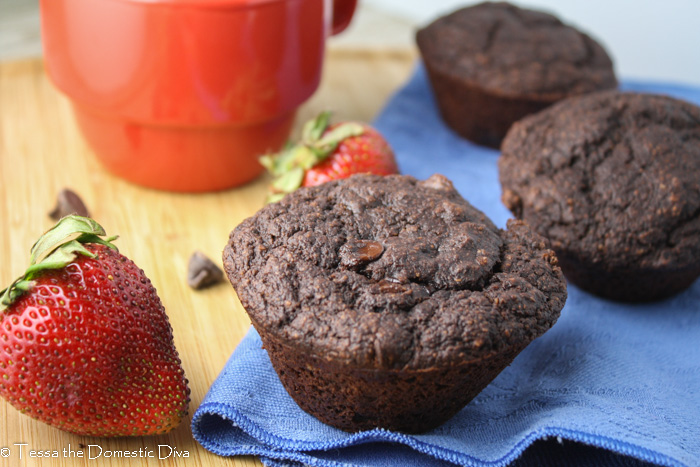 a close up of several double chocolate muffins arranged on a wood board with fresh strawberries