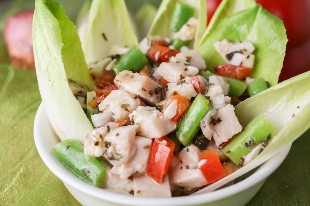 close up of chopped turkey, green bean, and red pepper slad in white bowl garnished with Belgian endive leaves