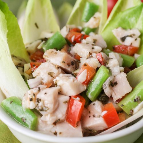 close up of chopped turkey, green bean, and red pepper slad in white bowl garnished with Belgian endive leaves