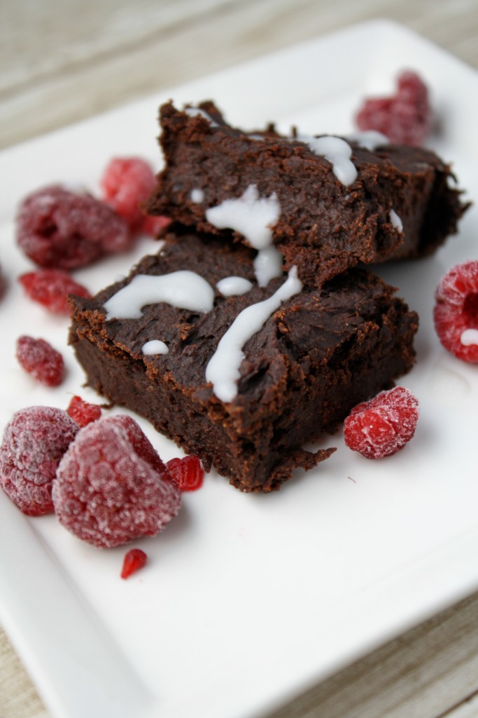 A square of cohoclate bean brownie on a white plate with frozen raspberries