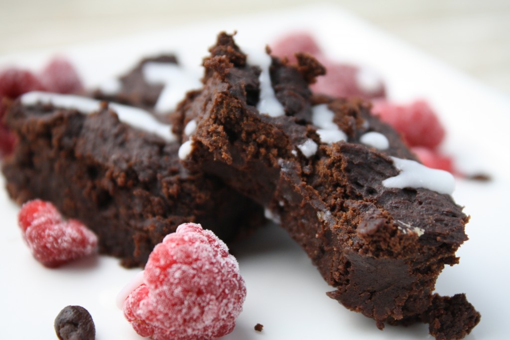 horizontal close up of a thick and fudgy brownie with a white plate with raspberries and a coconut butter drizzle