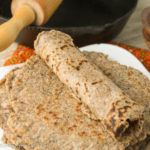 a stack of gluten free tortillas withn idividual rolled tortilla placed on top and a rolling pin and cast iron skillet in background