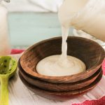 horizontal image of homemade coconut butter puring from a mason jar into a dark wooden bowl