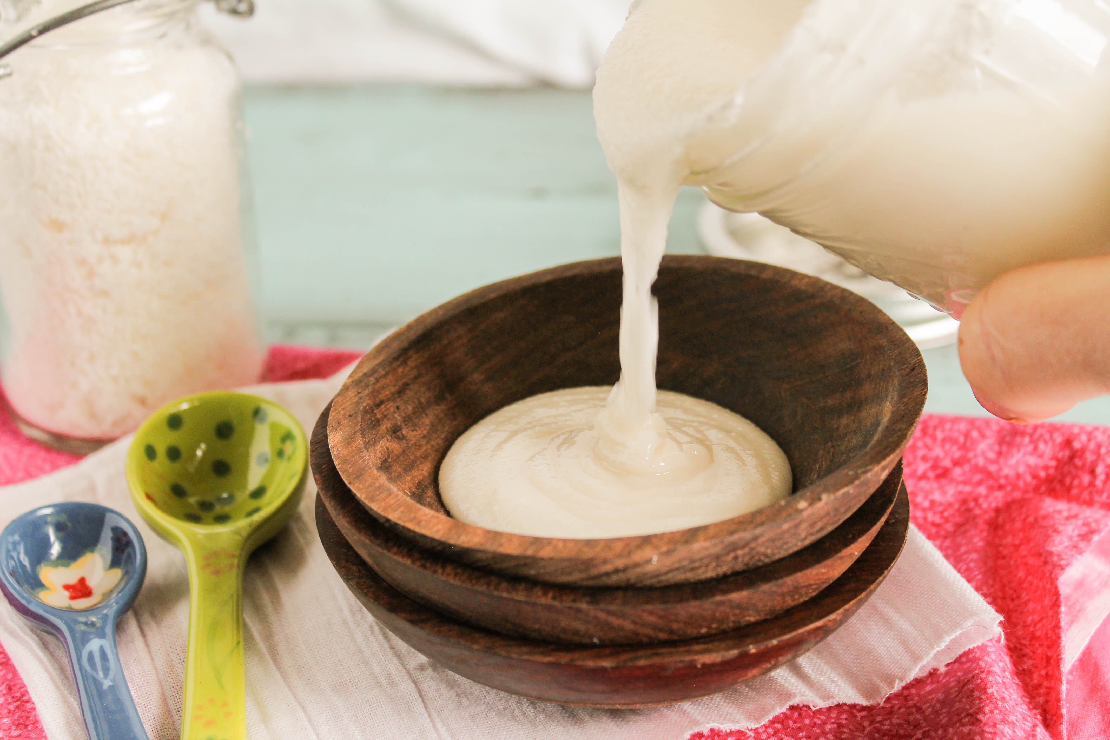 horizontal image of homemade coconut butter puring from a mason jar into a dark wooden bowl