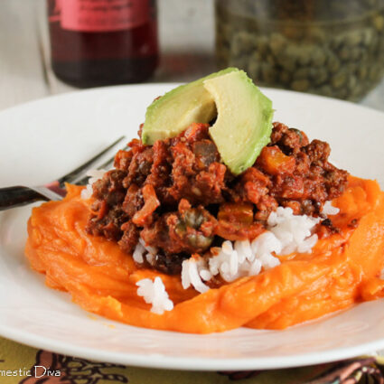 a bed of mashed sweet potatoes on a white plate with a topping of Cuban picadillo with ground beef