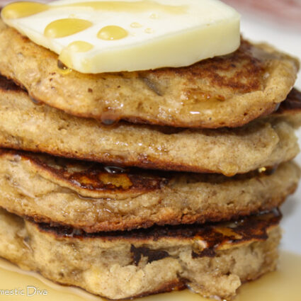 a stack of 4 pancakes with a pat of butter and maple syrup drizzle on a white plate