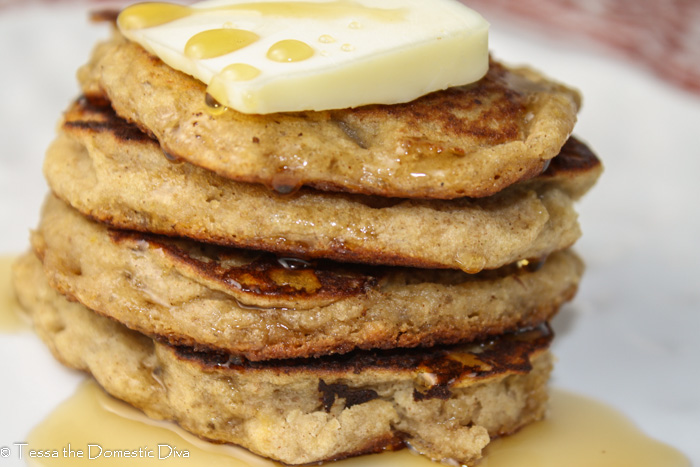 a stack of 4 pancakes with a pat of butter and maple syrup drizzle on a white plate