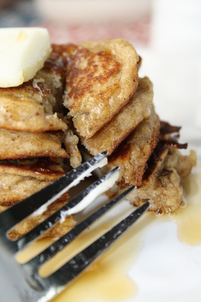 a fork slicing into a stack of 4 hearty wholegrain gluten free egg free pancakes with a pat a butter and a drizzle of maple syrup