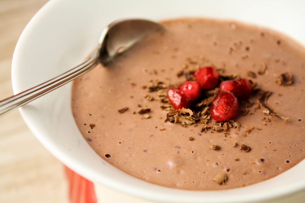 a close up of a thick and creamy chocolate mousse in a white bowl with a tapered bottom and a garnish of chocolate shavings and pomegranate seeds