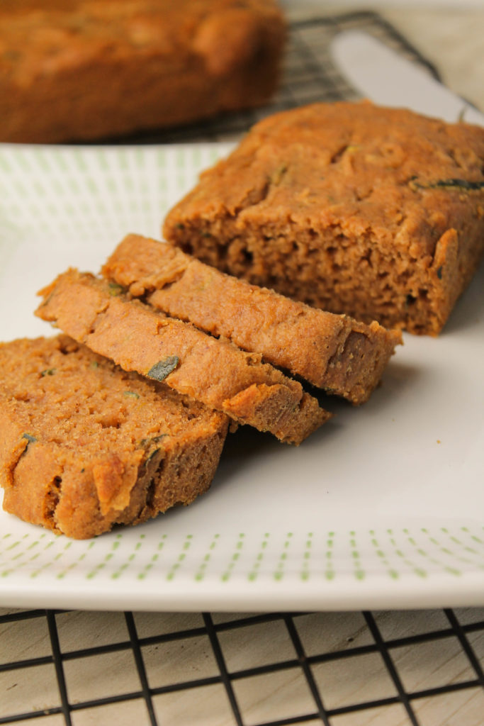 vertical image of sliced gluten free zucchini speckled bread on a white plate