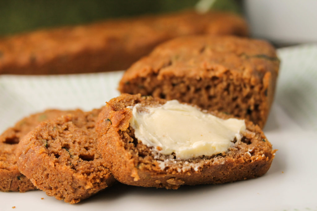 horizontal image of sliced gluten free began zucchini bread with a slathering of butter on a white plate at eye level