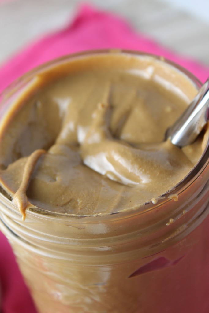 vertical image of creamy sunbutter in a glass mason jar with a pink background