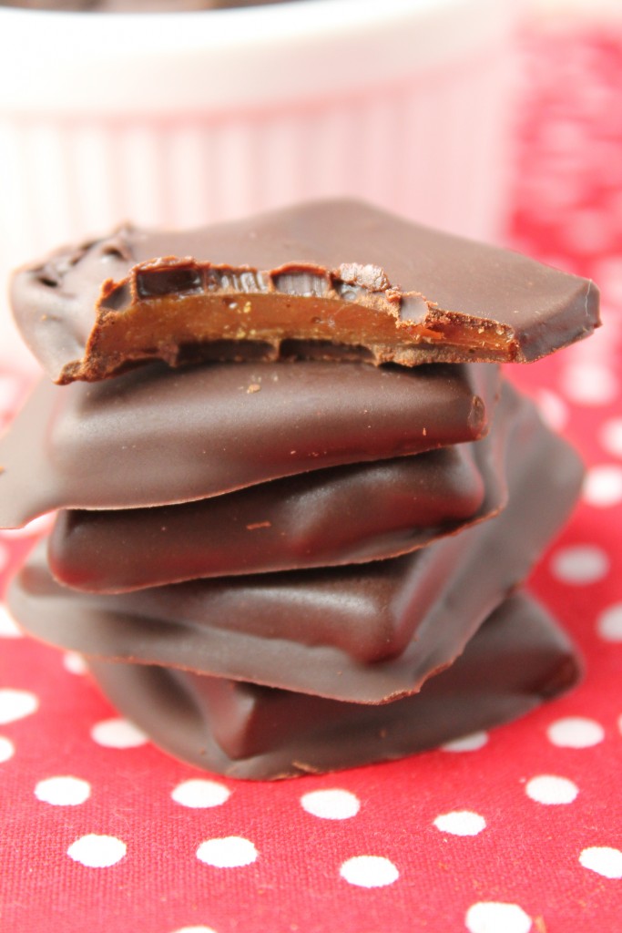 vertical image of paleo toffees coated in chocolate stacked on top of a red with white polka-dot cloth