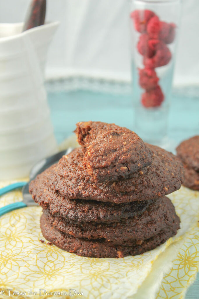 several stacked dark chocolate cookies with hazelnuts on a pale yellow cloth