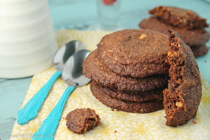 4 stacked chocolate hazelnut cookies from overhead atop a wooden surface with some fresh raspberries in the background