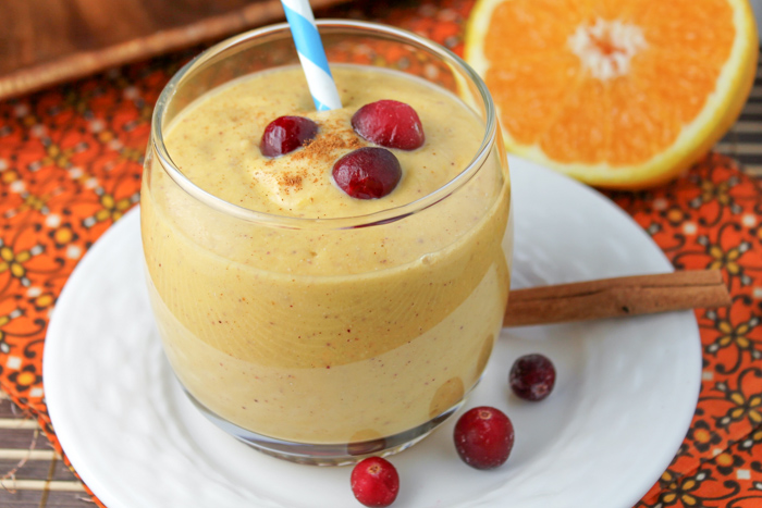 a small glass filled with a pumpkin smoothie topped with fresh cranberry and cinnamon