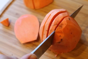 a peeled sweet potato being sliced with knife