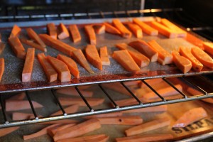 sweet potato fries evenly placed on a cookie sheet inside oven for baking