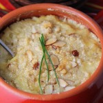 a circular red ceramic dish filled with baked artichoke dip with a almond and chive topping