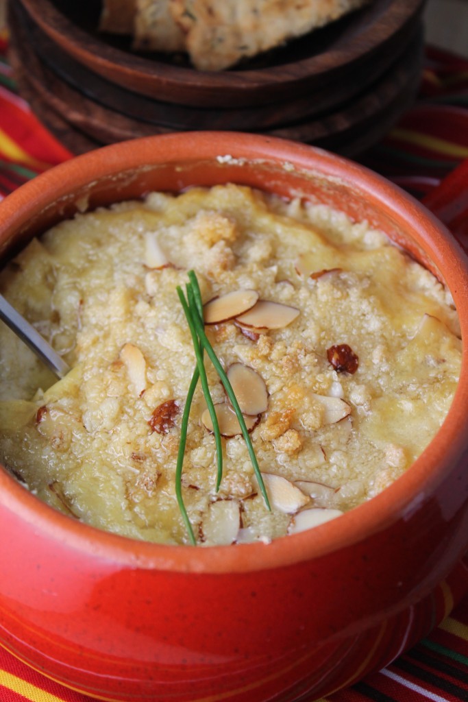 a circular red ceramic dish filled with baked artichoke dip with a almond and chive topping