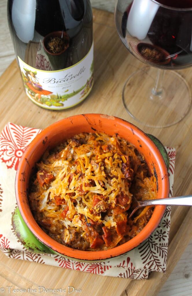 birds eye view of a green ceramic bowl filled with a spaghetti squash pizza casserole with a glass of red wine