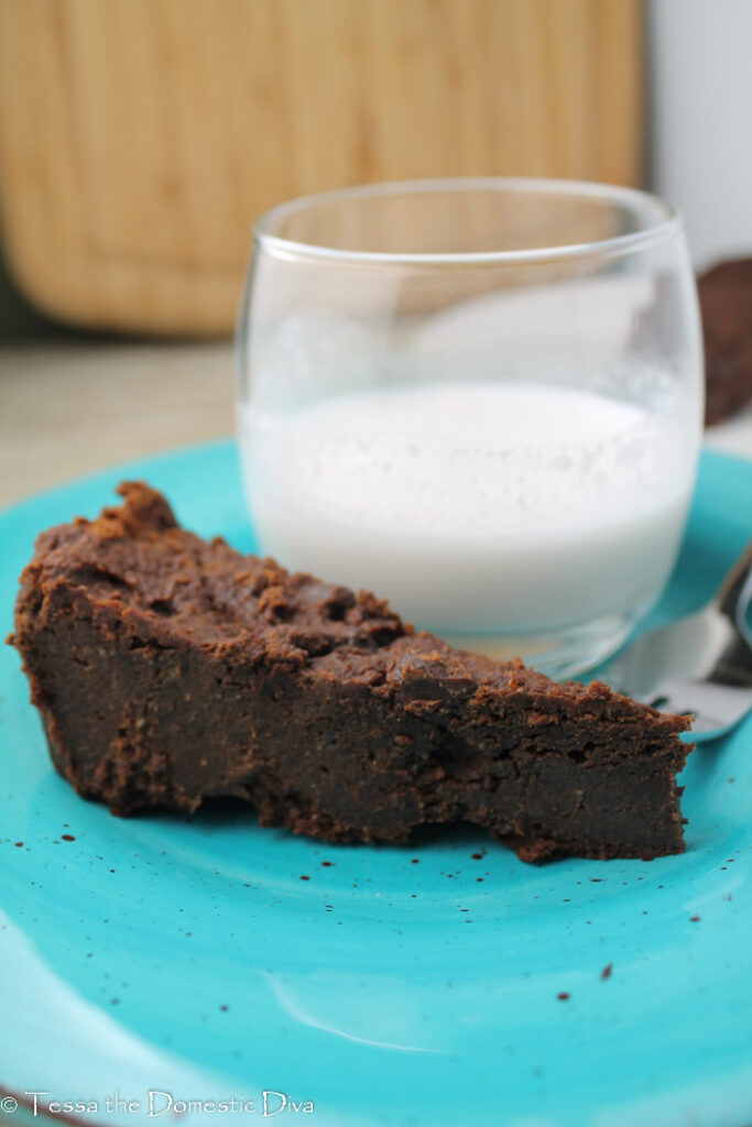 a slice of dense and fudgy gluten free vegan brownie on a blue plate with a glass of milk