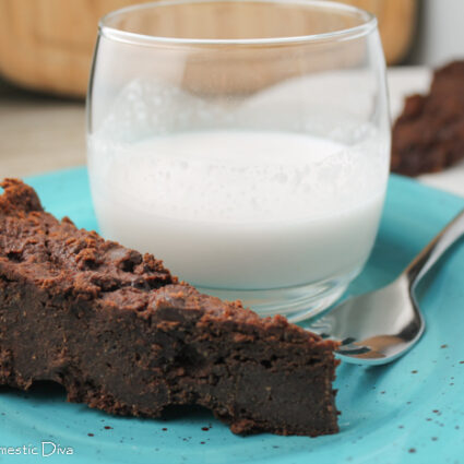 a triangle cut slice of vegan chococlate brownies on a blue plate with a cup of milk
